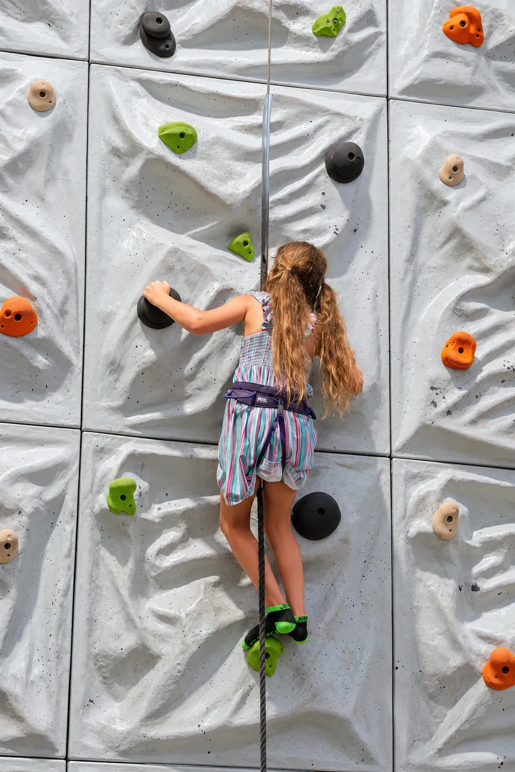 A child wearing a harness climbing the small rock wall at Fort Rock.