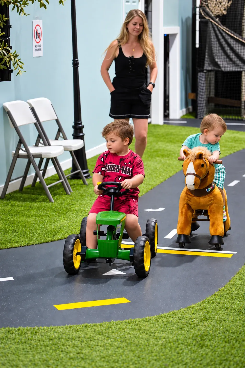 Two young children on a toy tractor and ride-on horse with a caregiver nearby.