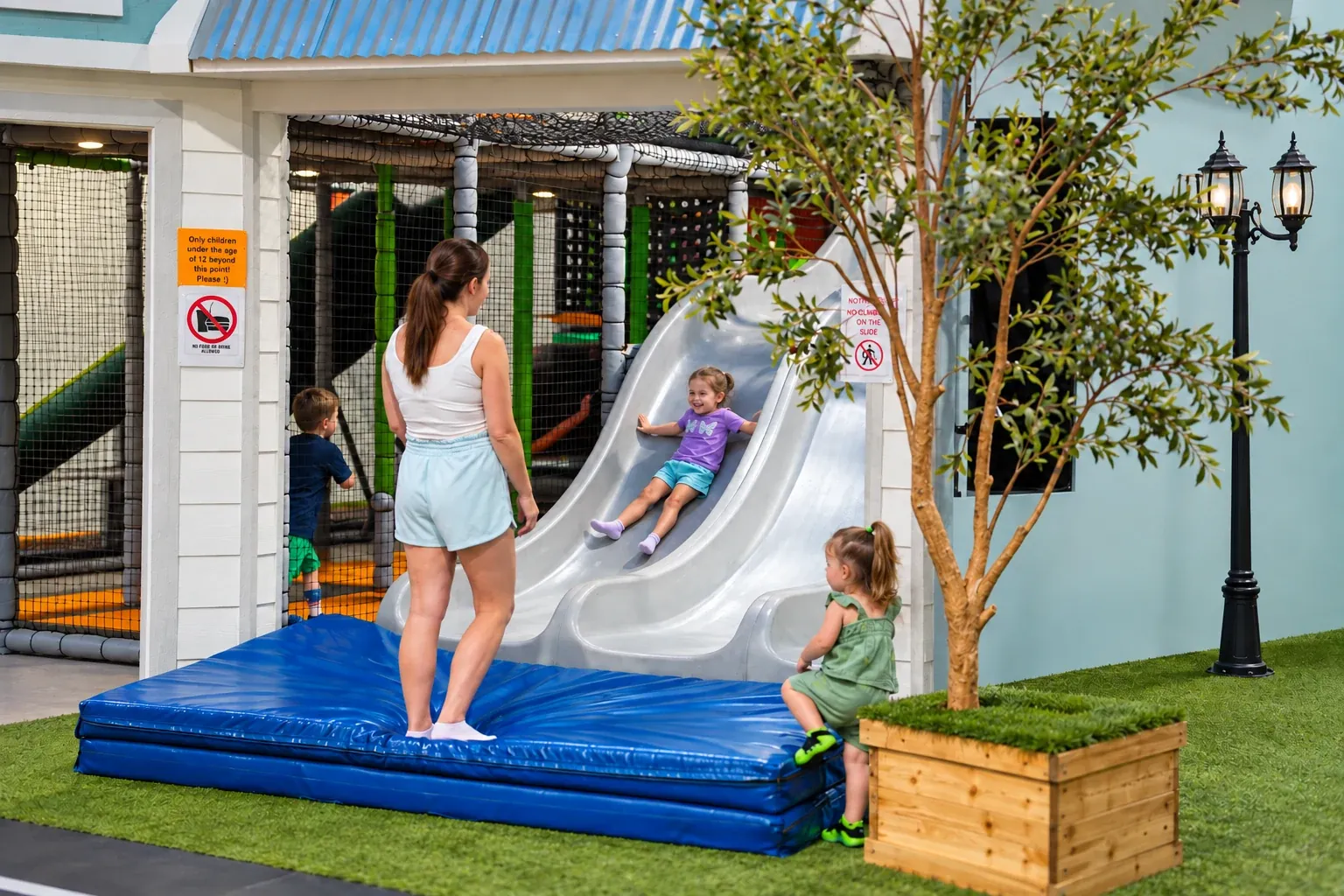 A child sliding down the indoor slide while a caregiver watches nearby.